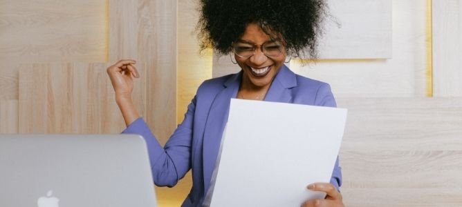 happy woman holding paper in front of laptop. happy woman holding paper in front of laptop.