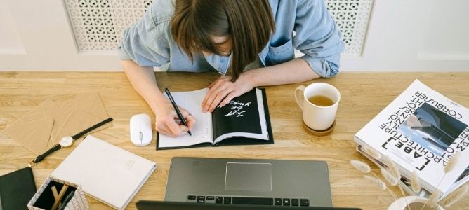 Woman taking notes in front of laptop. Woman taking notes in front of laptop.
