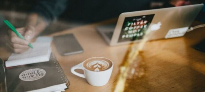 Person writing on a notebook with coffee.