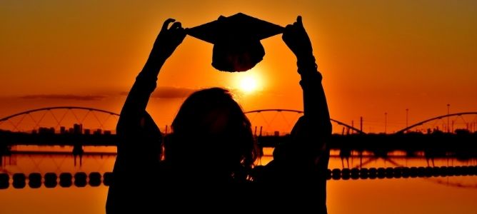 Silhouette of person holding graduation cap over head at sunset in front of a bridge. Silhouette of person holding graduation cap over head at sunset in front of a bridge.