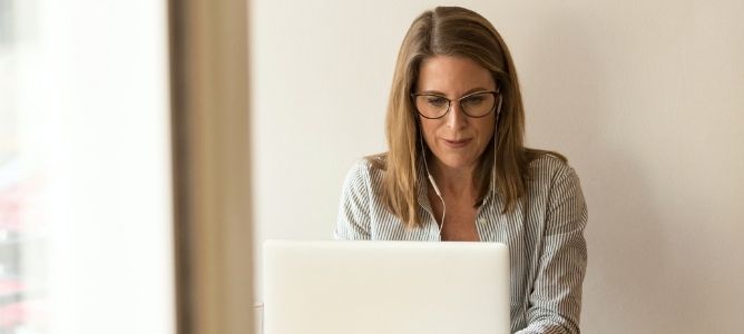 Two women standing and one woman sitting looking at a computer screen with bookshelves and an American flag in the background. Two women standing and one woman sitting looking at a computer screen with bookshelves and an American flag in the background.