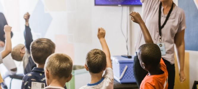 Children raising their hands in classroom.