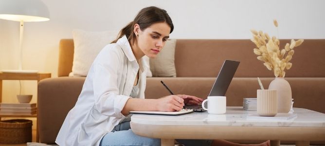 Woman taking notes and using laptop.