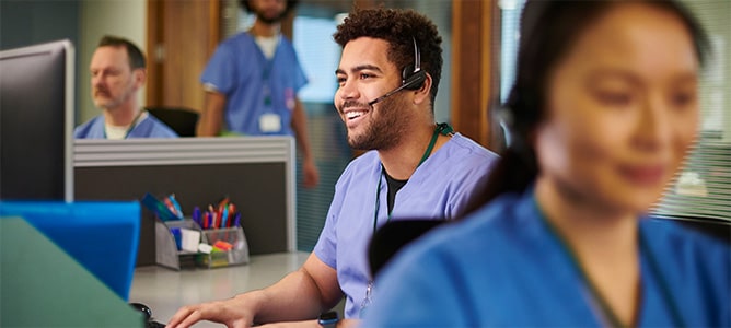 Man in blue scrubs with headset in medical office.