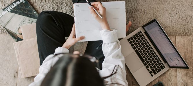 Girl sitting on the floor with a laptop writing in a planner. Girl sitting on the floor with a laptop writing in a planner.