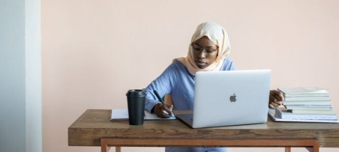 Woman studying and taking notes at her desk with a laptop.